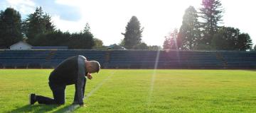 Coach Joe Kennedy kneels on the football field at Bremerton High School in Washington