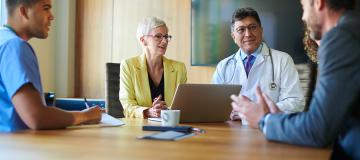 A group of doctors and other health-care professionals sit around a table