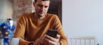 A man sits at a table reading from his mobile phone