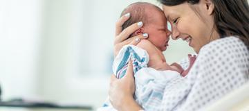 A mother smiles and holds her newborn baby