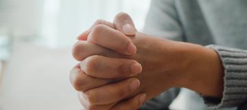 A person sits with their hands clasped