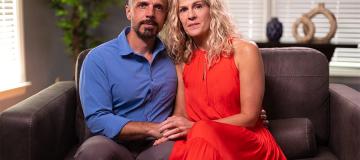 Dan and Jennifer Mead sit on a leather couch looking into the camera