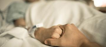 A woman in a hospital bed holds a man's hand