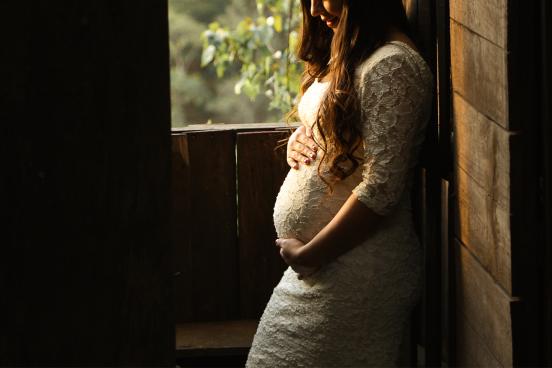 A pregnant woman stands by a window.