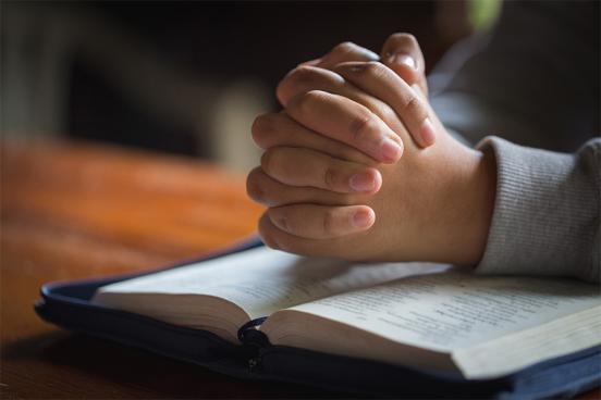 Folded hands praying over the bible