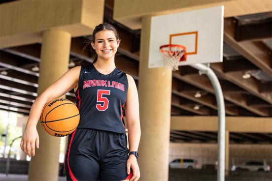 Amelia Ford holds a basketball on the court with a hoop in the background