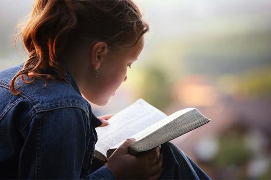 Girl in a jean jacket reading the Bible