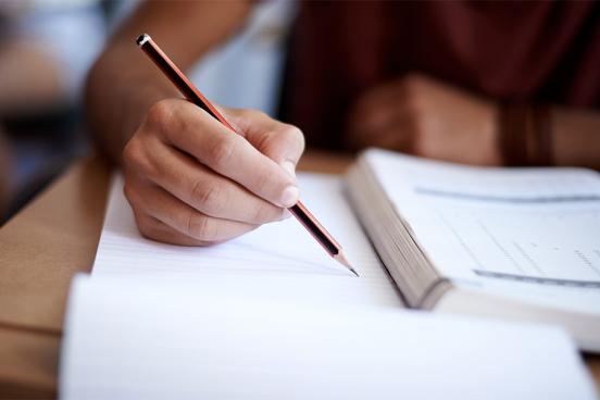 Student Writing on paper while reading a textbook