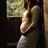 A pregnant woman stands by a window.