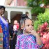 A foster child in a purple dress stands outside a brick house