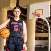 Amelia Ford holds a basketball on the court with a hoop in the background