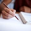 Student Writing on paper while reading a textbook