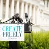 Microphones sit on a podium with a sign that reads 'Create Freely' in front of the U.S. Capitol